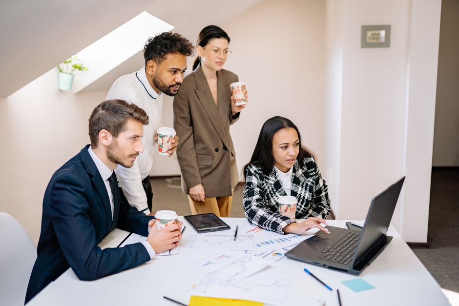 Uma equipe diversificada colabora em um escritório moderno, utilizando laptops e tablets para planejamento e brainstorming.
