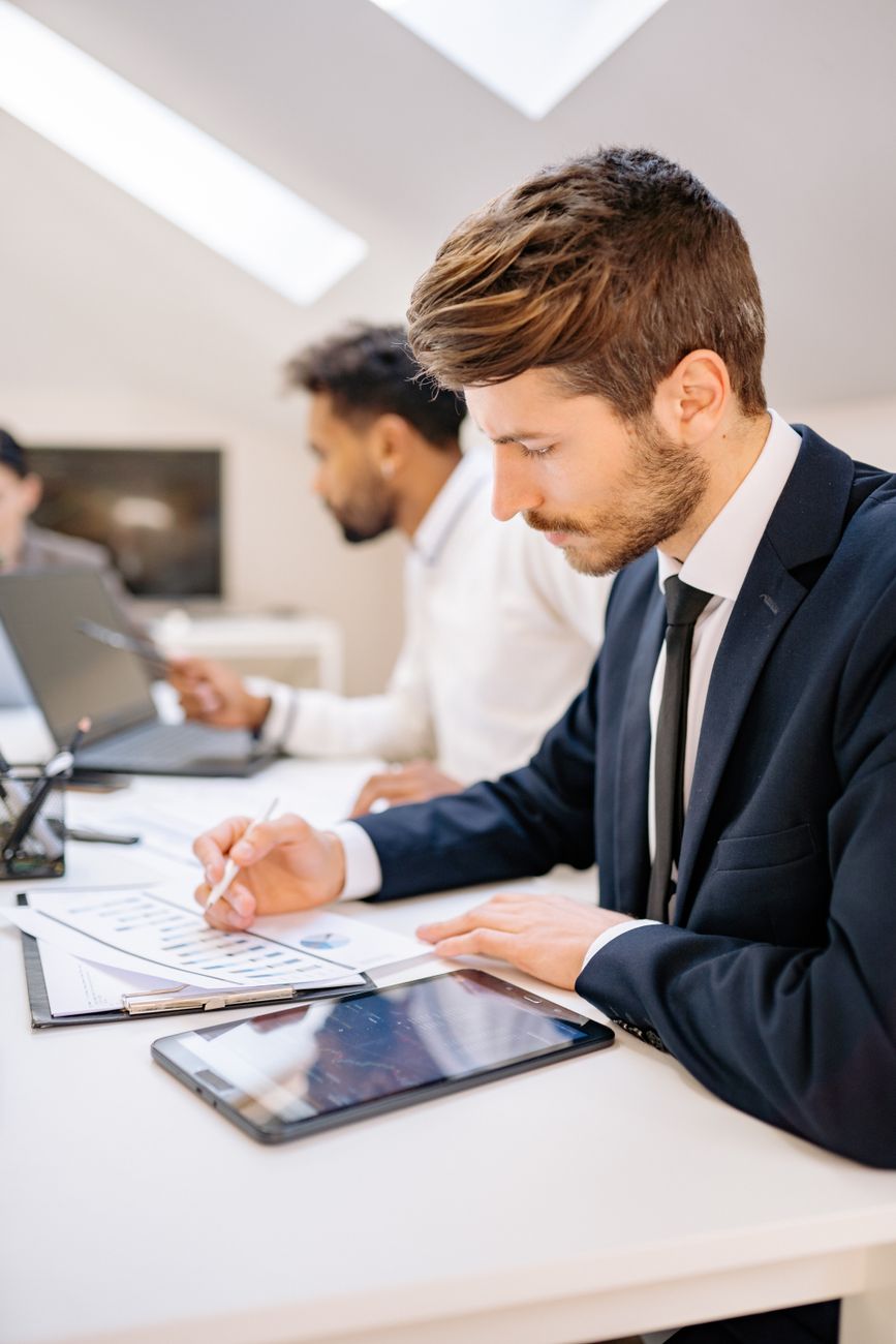 Two men in an office reviewing documents and using a tablet for work.