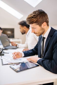 Two men in an office reviewing documents and using a tablet for work.