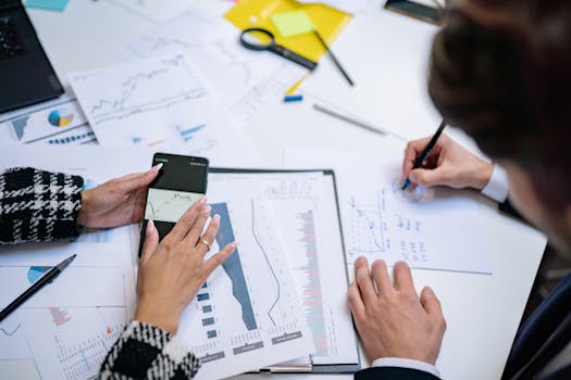 Overhead view of people analyzing financial graphs and data with smartphone and documents.