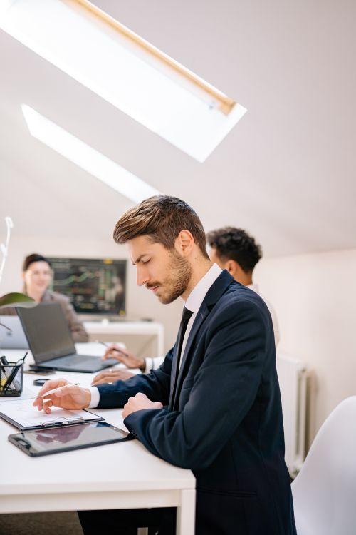 Free Business professionals in a modern office setting working on tablets and laptops, showcasing teamwork and productivity. Stock Photo