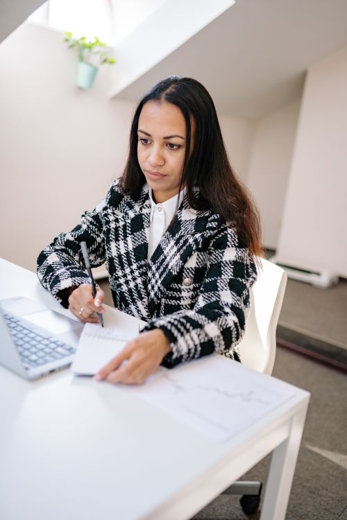 Free Focused businesswoman writing notes at her office desk with a laptop. Stock Photo