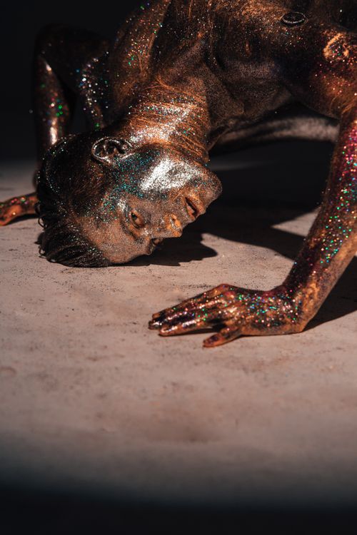Free A performer with glitter body paint in a dynamic dance pose, symbolizing strength and art. Stock Photo