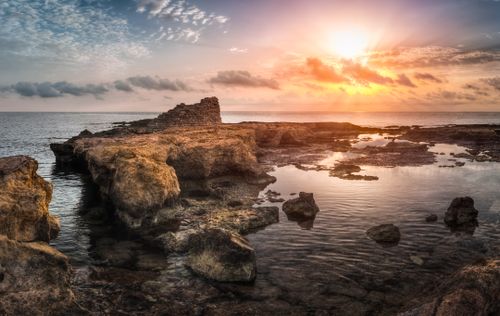 Free Dramatic sunset over a rocky shoreline with clear reflections and vibrant colors. Stock Photo
