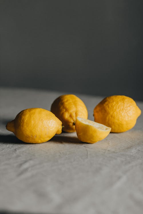 Whole and sliced ripe lemons placed on table with tablecloth against gray background in room