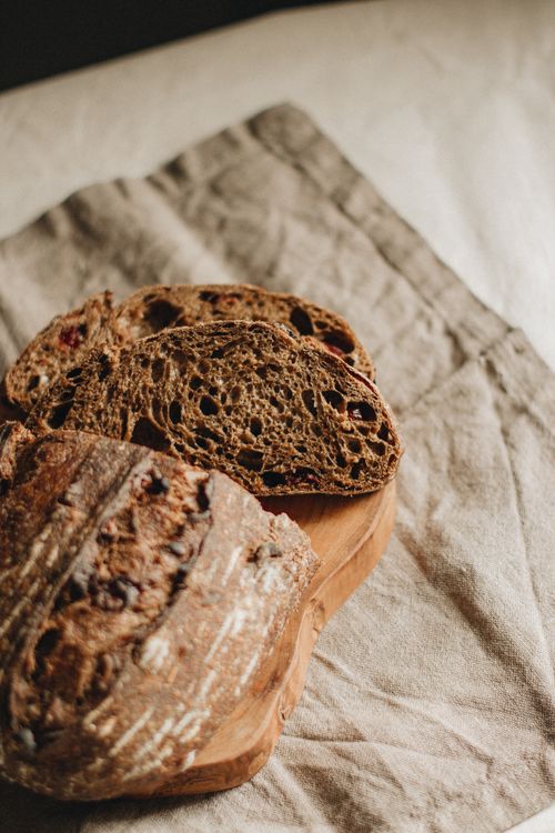 Free From above of cut loaf of freshly baked cranberry whole wheat black bread placed on crumpled napkin in light room Stock Photo