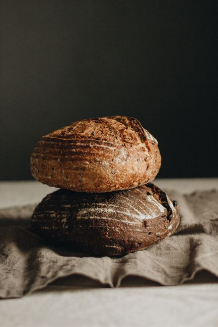 Delicious freshly whole baked loaves of bread placed on each other on crumpled napkin against black background in light studio