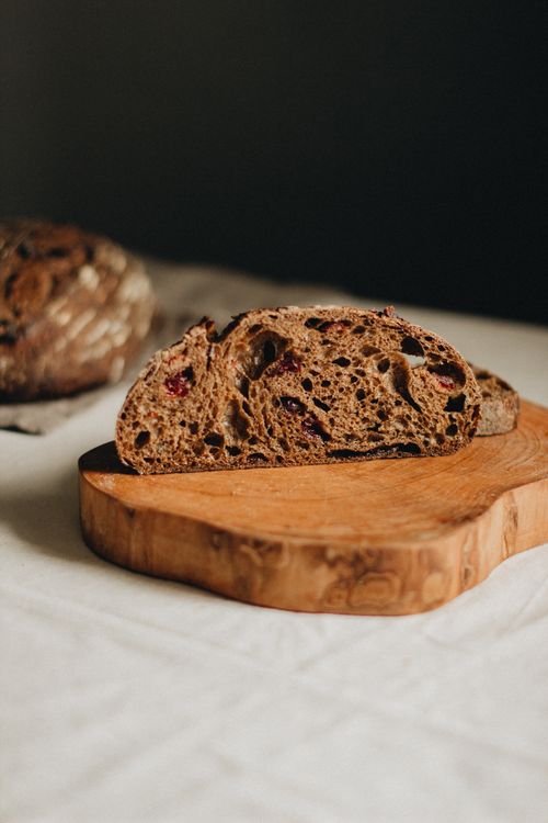 Free Sliced of tasty cranberry whole wheat bread placed on wooden cutting board on table against black background in light studio Stock Photo