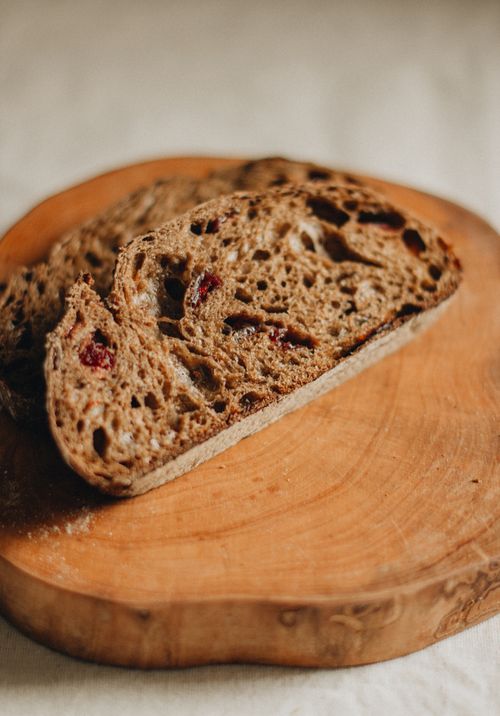 Free Slices of freshly baked cranberry black bread placed on round wooden chopping board on white table in light room in studio Stock Photo