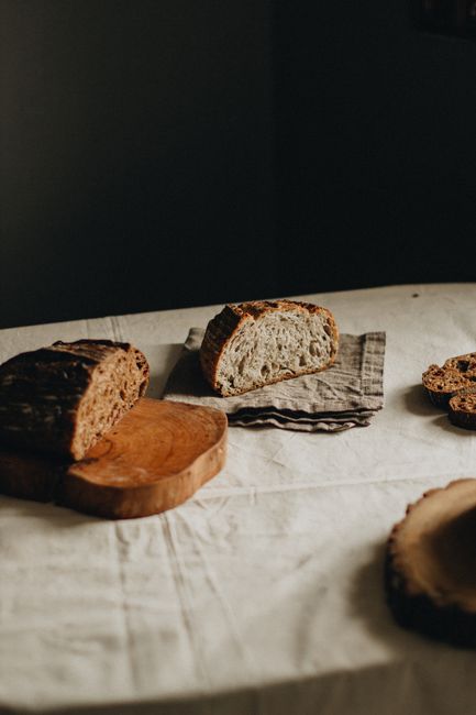 Loaves of black and white bread cut in halves placed on wooden cutting board and napkin on black background in studio