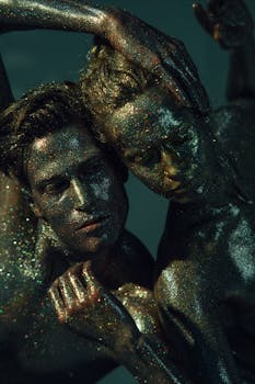 Two glitter-covered models posing in an artistic composition, captured up-close with dramatic lighting.
