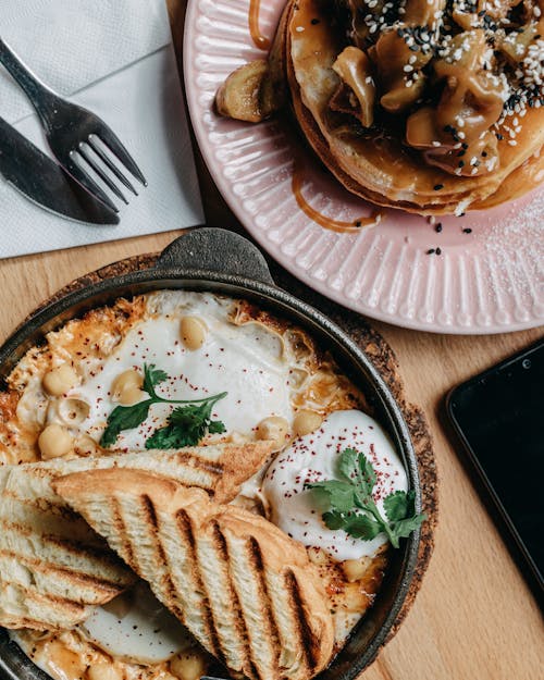 Free From above of delicious potato egg skillet with seasoning and bread placed near plate with pancakes with sweet cream on table in daytime Stock Photo