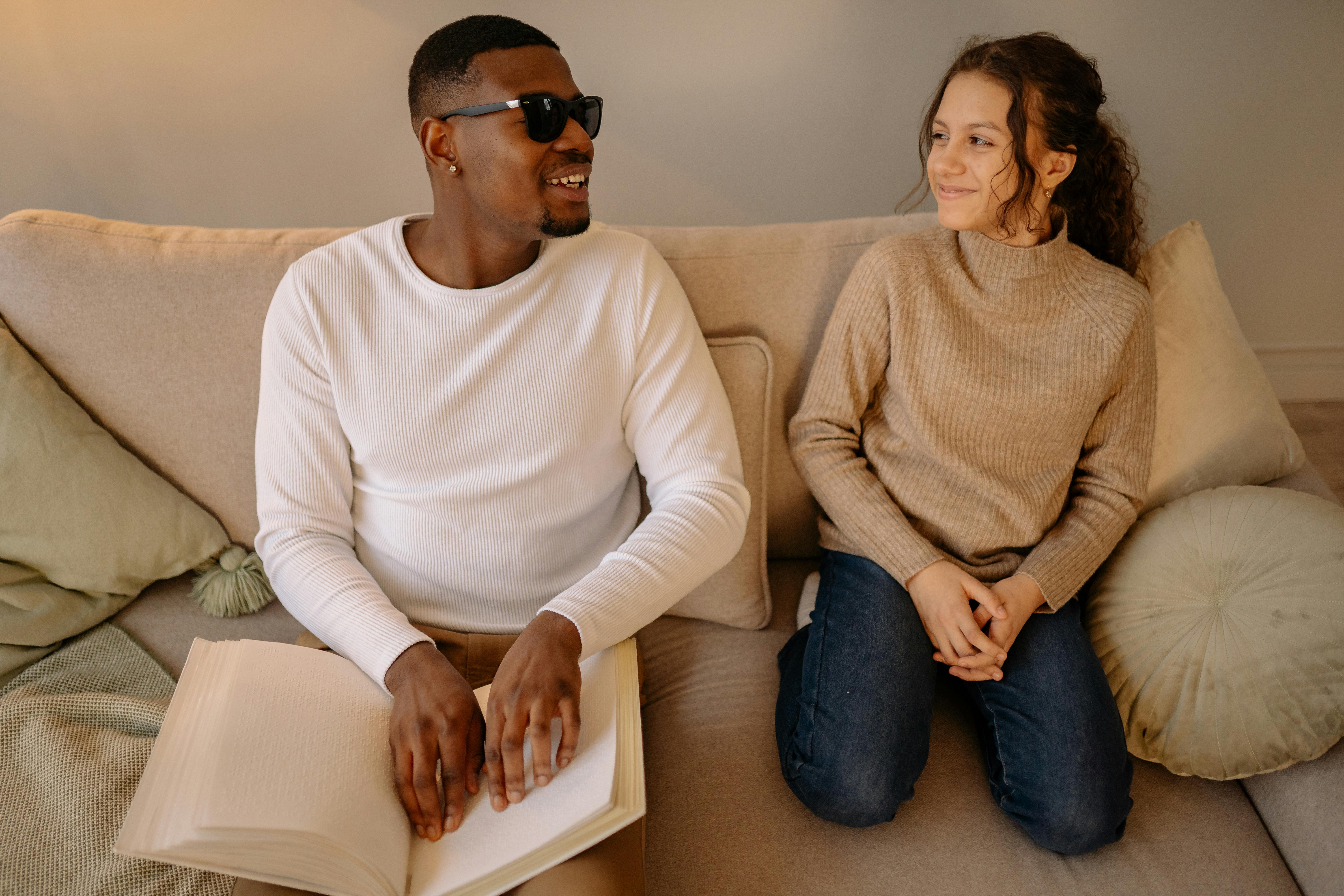 a girl sitting beside a man holding a white book