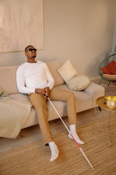 A man with sunglasses sits on a sofa holding a walking stick in a stylish living room.