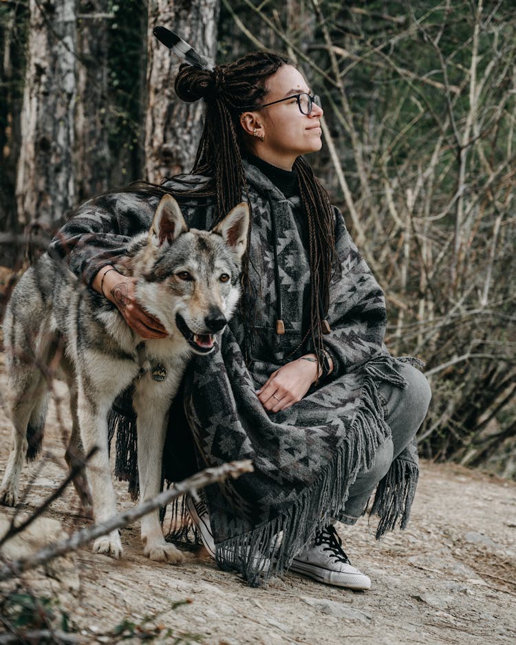 Female In Poncho Squatting Down Near Wolf In Nature