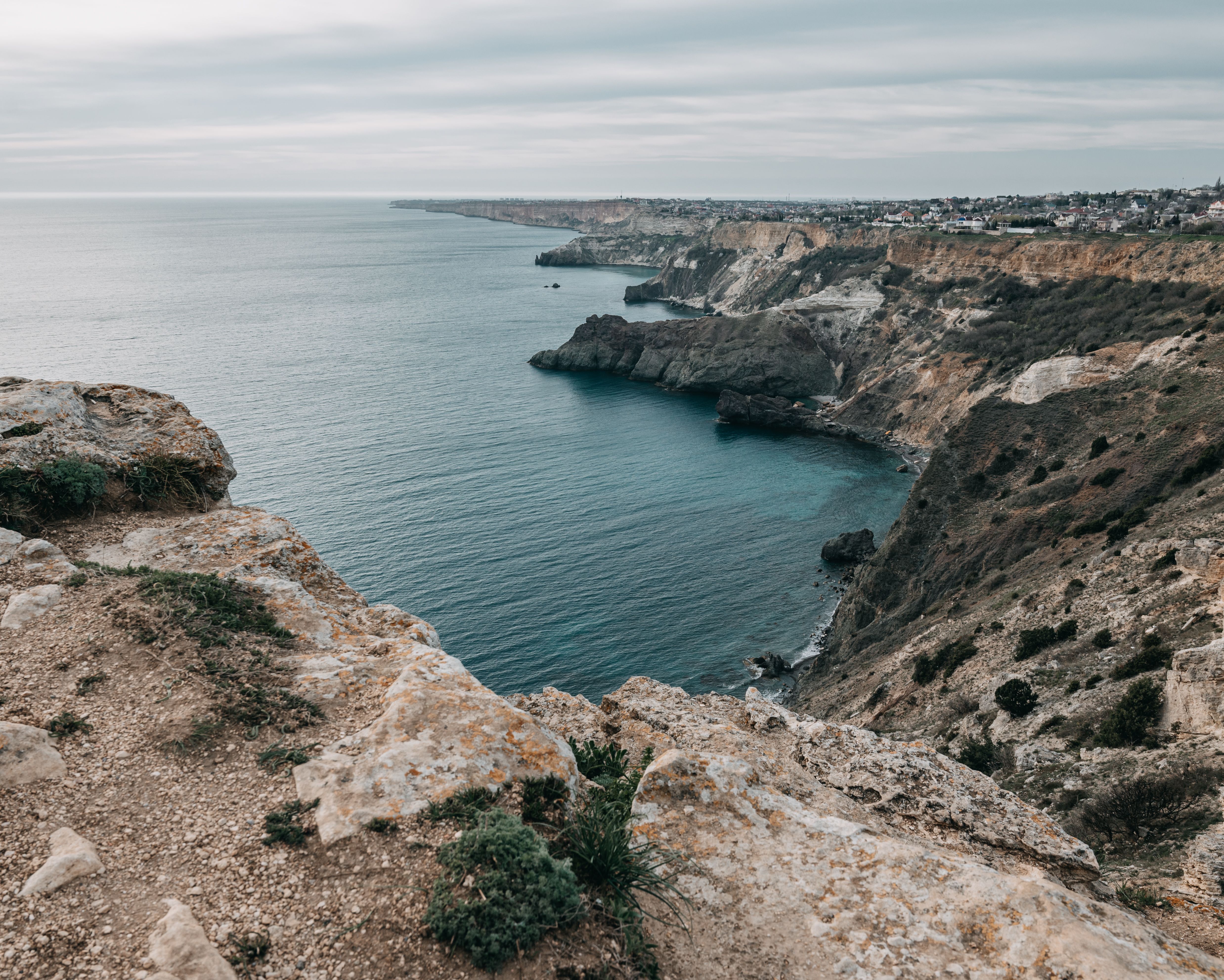 Picturesque rough cliffs washed by calm endless water of ocean under cloudy gray sky