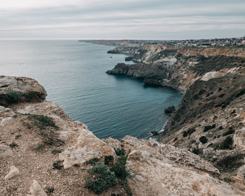 Picturesque rough cliffs washed by calm endless water of ocean under cloudy gray sky
