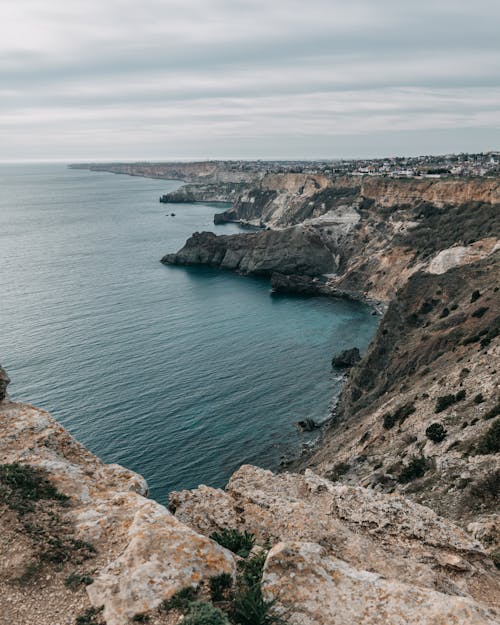 Spectacular rough terrain surrounded with rippling water of ocean under cloudy gray sky