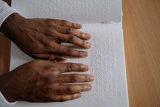 A close-up view of hands reading an open book with Braille alphabet.