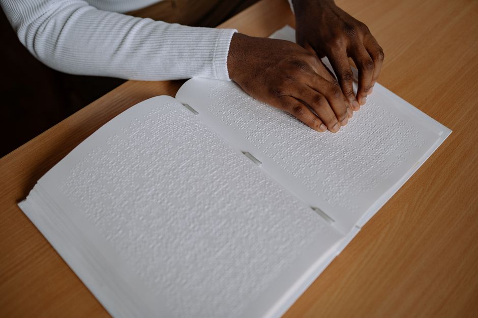 Close-up of hands reading a Braille book, symbolizing accessibility and inclusion.