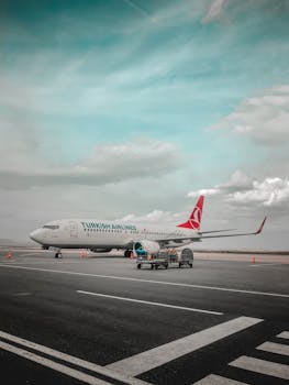 Turkish Airlines plane parked on airport tarmac with clear blue sky and clouds.