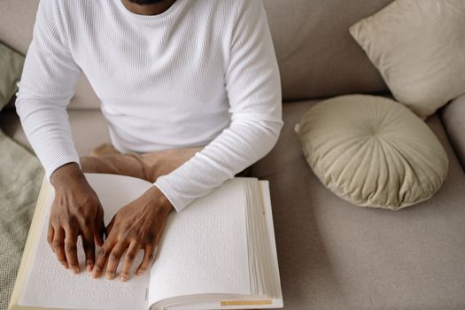 A person in a white sweater reads a Braille book on a comfortable couch, highlighting tactile learning.