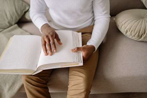 Free A Person Sitting on Gray Couch Holding Braille Book Stock Photo