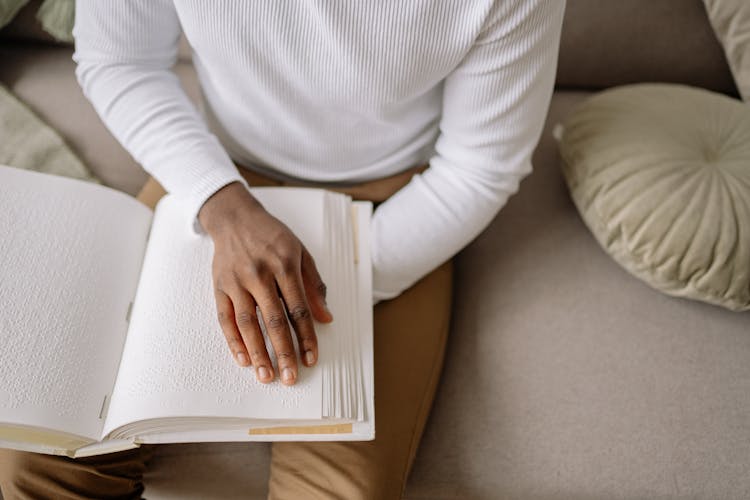 A Person Reading A Braille Book On A Couch