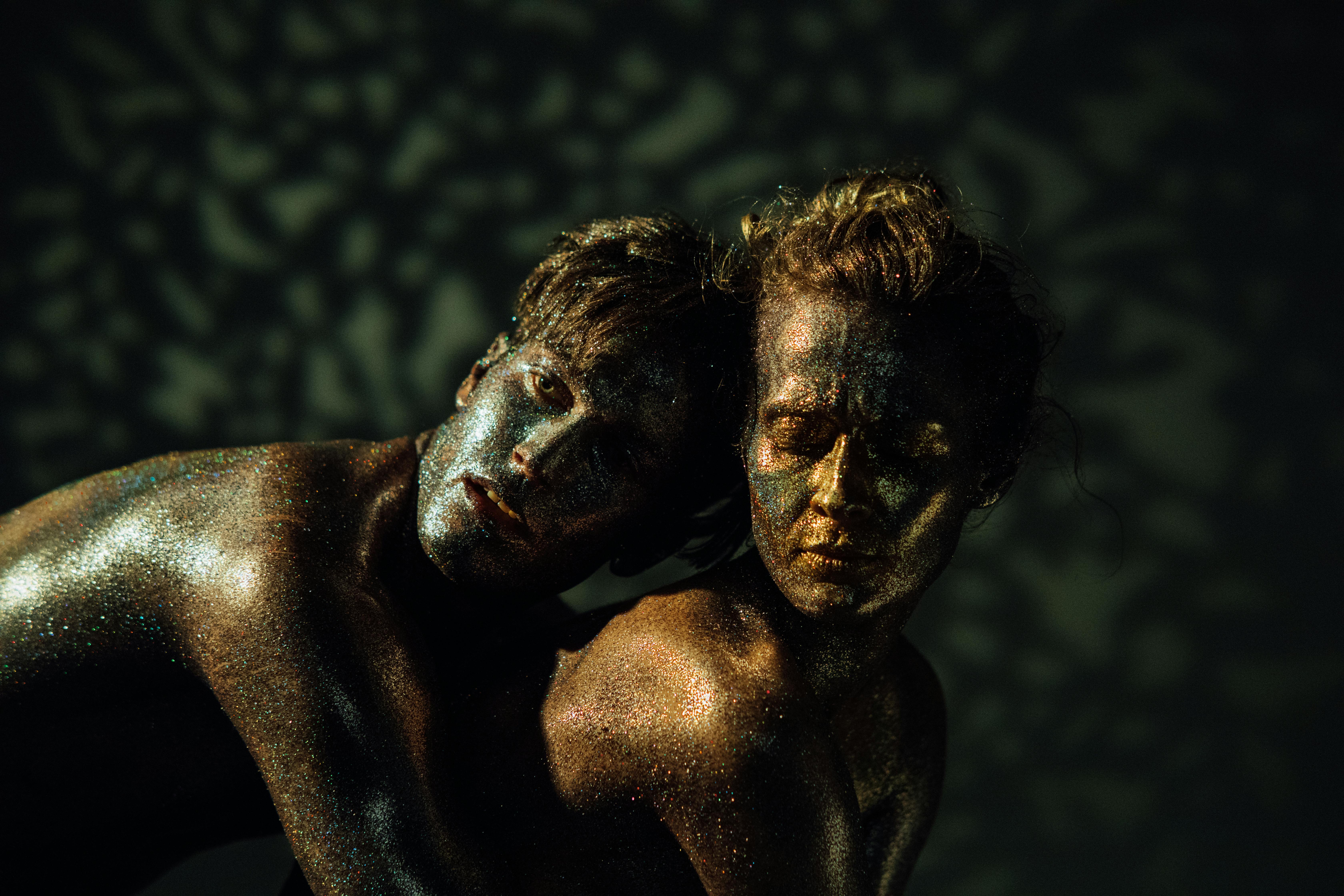 Free Dynamic duo adorned in glitters showcases an artistic dance performance with dramatic lighting. Stock Photo