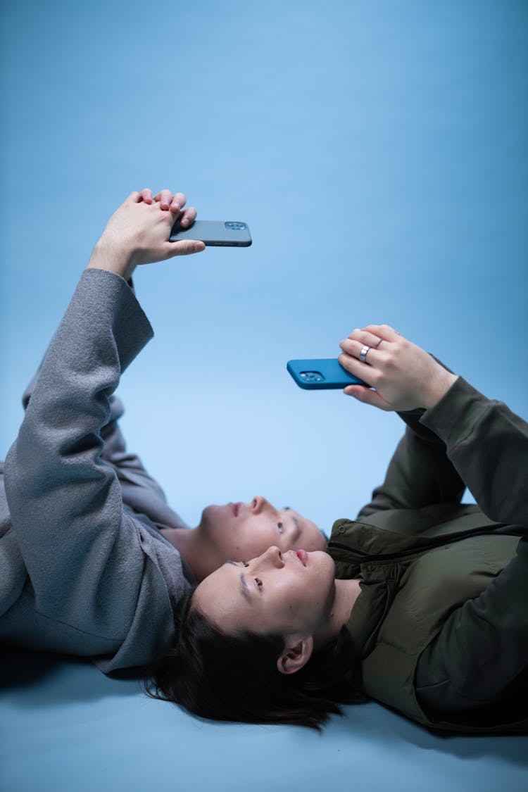 Brothers Lying On The Floor While Using Cellphones