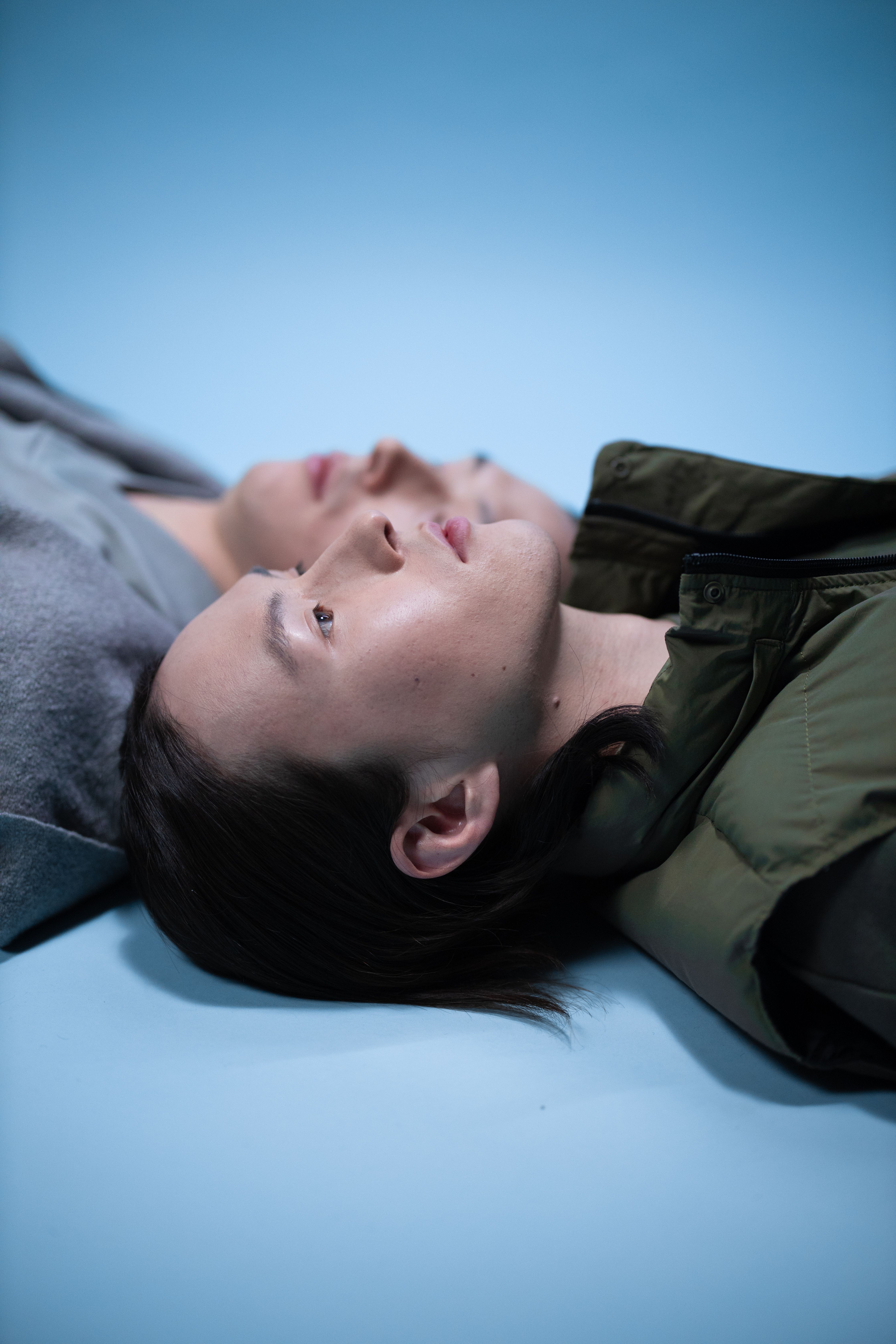 Two young adults lying down on a blue surface, looking thoughtful.