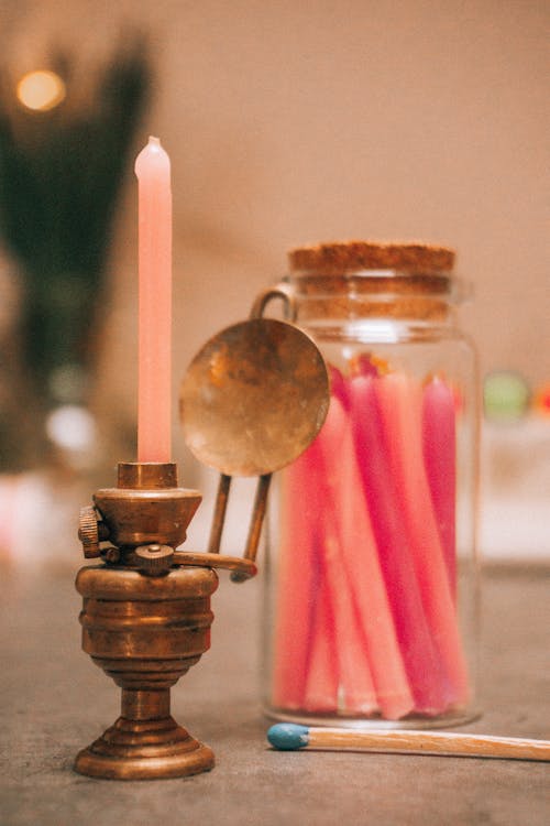 Set of decorative candles placed in glass jar near candleholder with flaming candle in festive room against blurred background