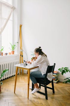 Teen girl studying at a desk in a well-lit room with plants, focused on online learning.