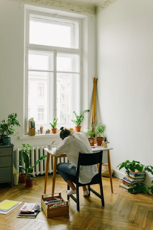 Back View of a Person Sitting on Black Chair while Doing Her Homework on the Table