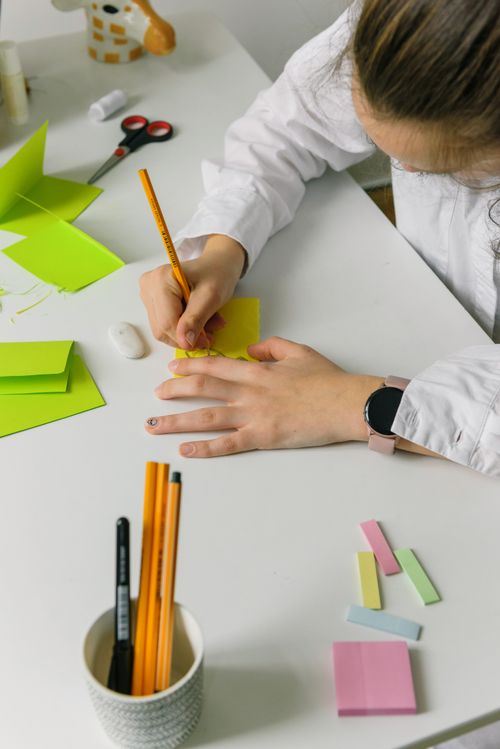 Free Top view of a woman writing notes with pencil on colorful paper at an office desk. Stock Photo
