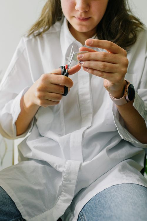 Free Close-up of a young woman cutting paper with small scissors indoors. Stock Photo