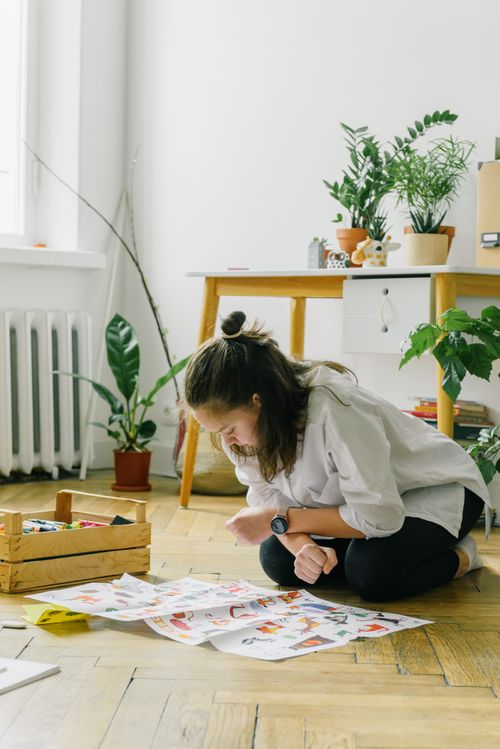 Free Woman sitting on floor in a plant-filled room reviewing art papers. Stock Photo