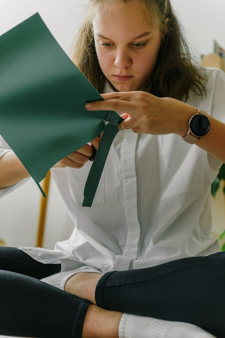 A Young Woman In White Dress Shirt Cutting Green Paper