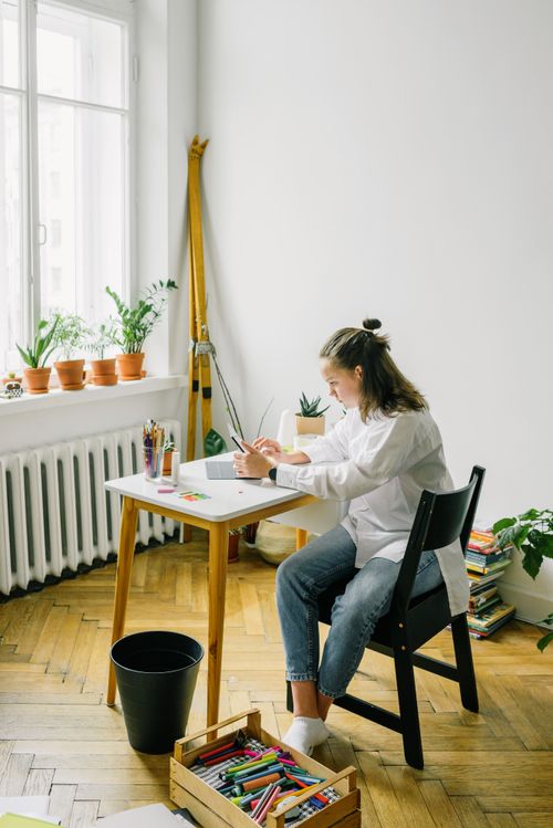 Free Adult woman focused on a digital project at home, sitting by a window with plants. Stock Photo