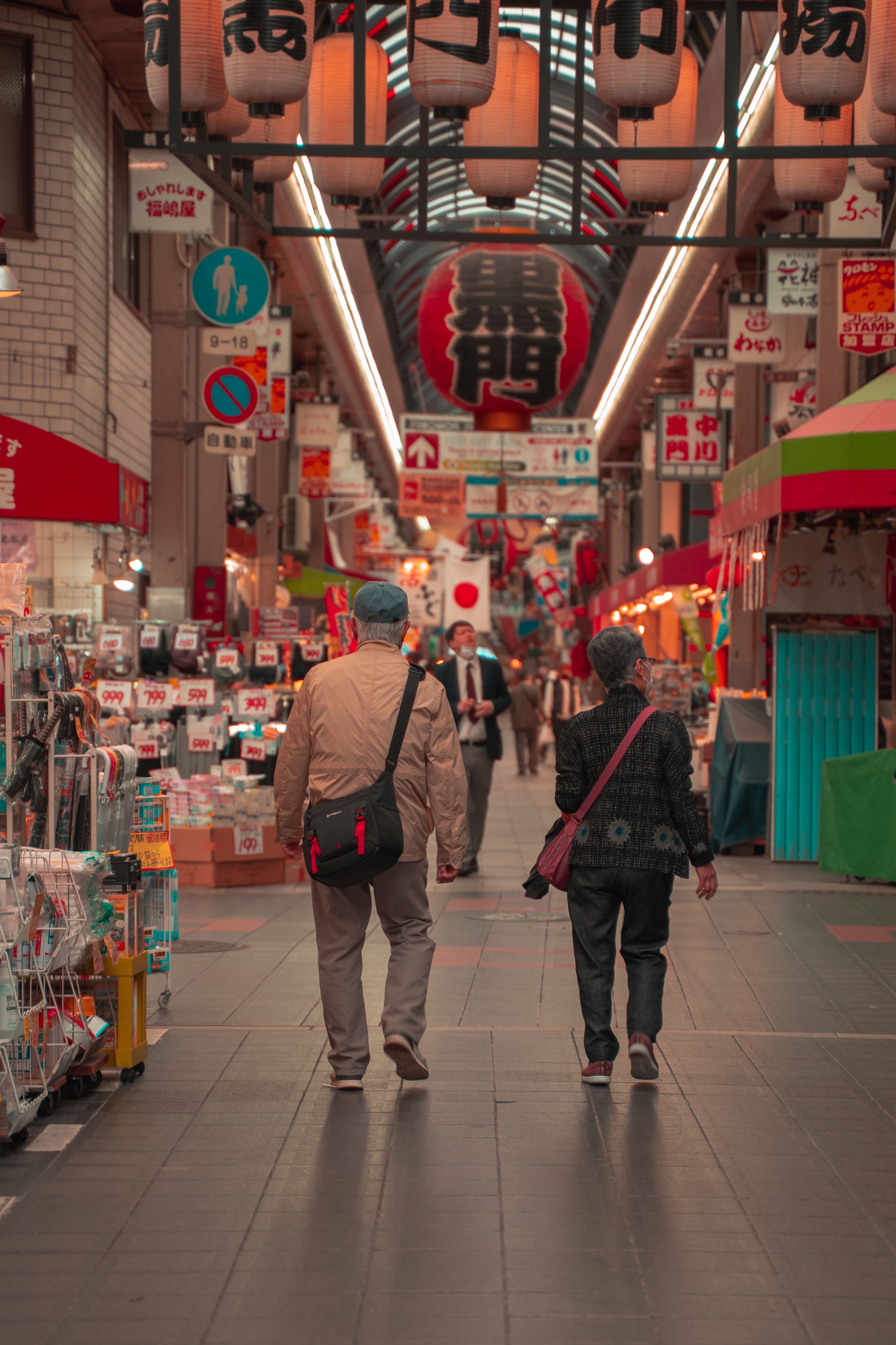 Elderly couple walking through a Japanese indoor market with traditional lanterns overhead