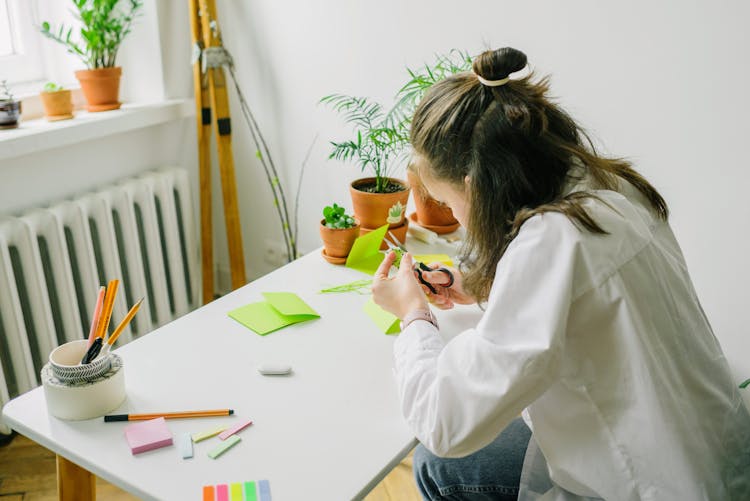 A Person Sitting At A Desk Cutting Green Paper