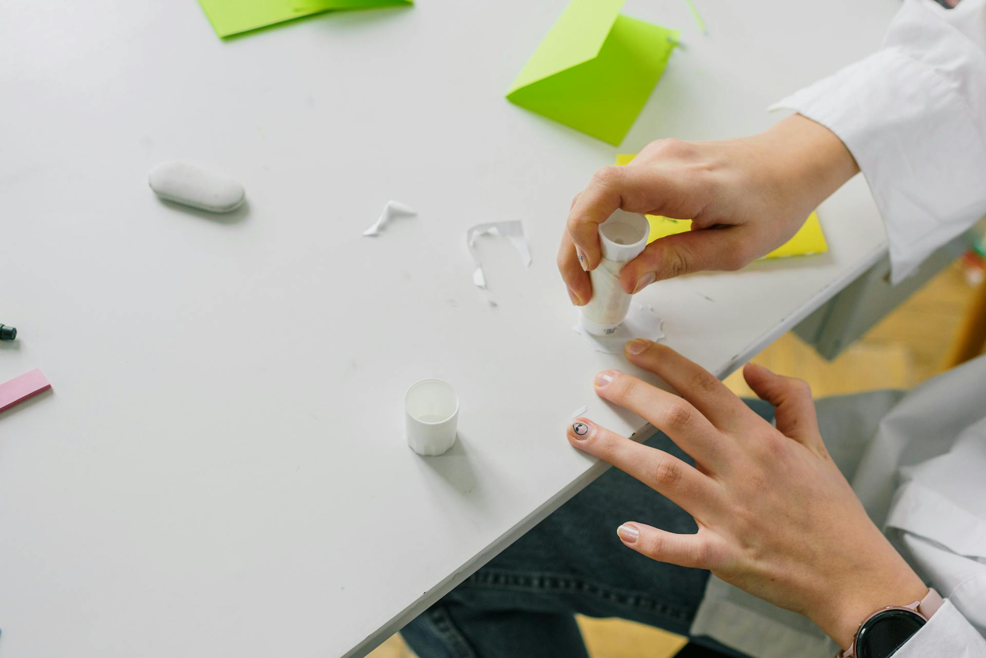 Close-up of hands applying glue stick on paper for a craft project on a desk.