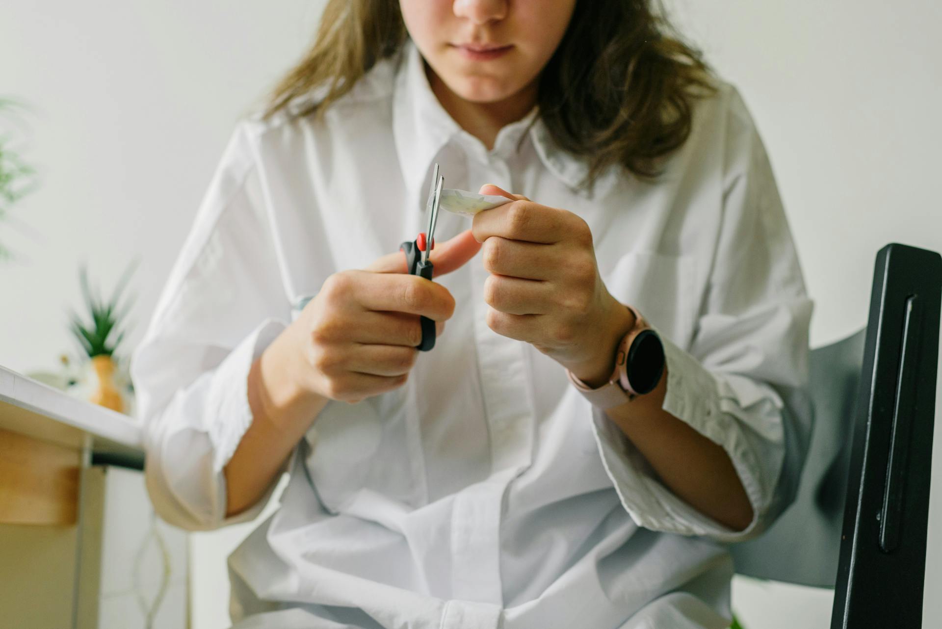 Close-up of a woman cutting paper indoors, focused on hands and scissors.