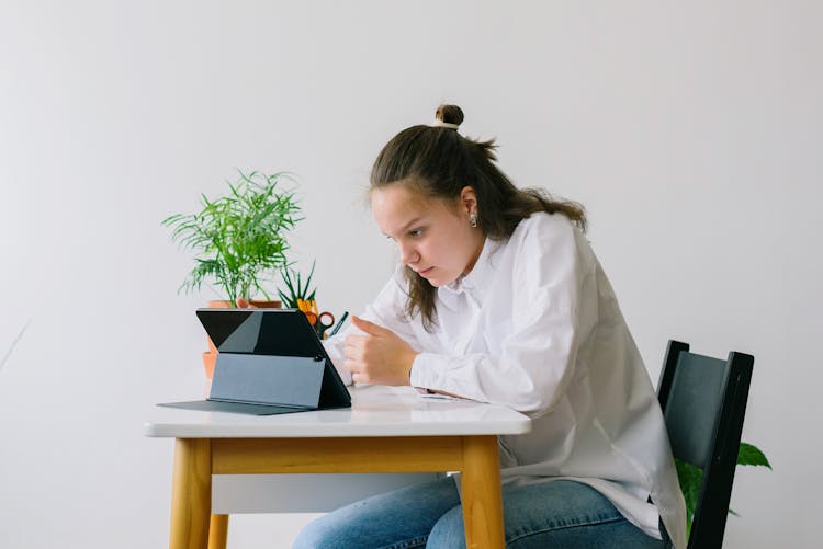 Teenage Girl In White Long Sleeve Shirt Looking At The Screen Of A Tablet