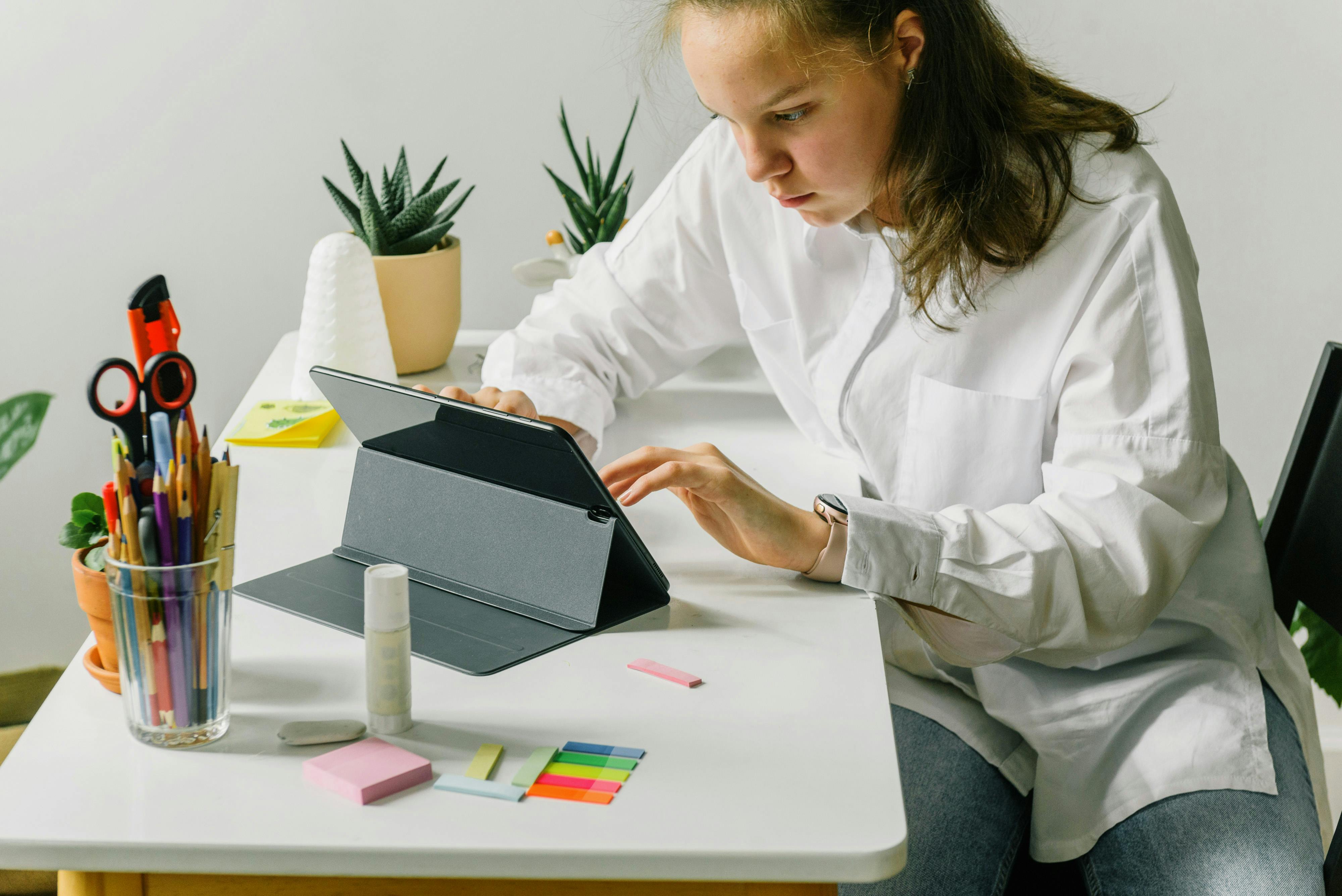 Teenage girl using tablet on desk with school supplies, focusing on digital learning.