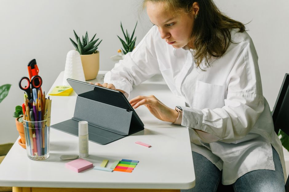 Teenage girl using tablet on desk with school supplies, focusing on digital learning.