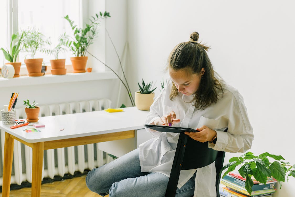 Free A Teenage Girl Using a Tablet while Sitting in a Chair Stock Photo
