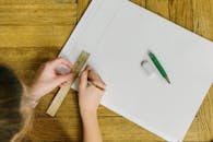 A Person Writing on Paper while Using a Ruler and Pencil