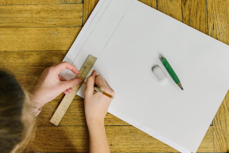 A Person Writing On Paper While Using A Ruler And Pencil