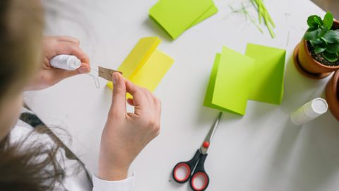 A person engaged in crafting, folding vibrant papers with tools on a desk.